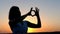 A Young Sportive Woman Makes a Love Gesture at a Splendid Sunset