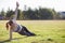 Young sportive woman in sports clothes training in field at sunrise. Girl standing in plank position on grass in a city park