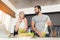 Young sports couple is preparing in the morning in the kitchen. A man is making a green vegetable cocktail.