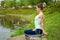 A young sports girl practices yoga on a green lawn by the river, yoga asana posture. Meditation and unity with nature