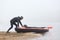 Young sportsman being ready rowing canoe, pushing boat into water, kayaker in warm clothes, padding in early fogging morning,