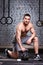 Young sportsman crouching on a one leg and holding kettlebell against brick wall in the cross fit gym.