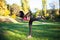 Young sportswoman doing warm-up balance exercise standing on one legs stretching leg and back outdoors. Warm-up stretching at the
