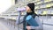 Young sportswoman holding rolled-up exercise mat in hands and drinking water while working out on sports ground