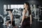 Young sportswoman lifting weights in gym wearing sportswear with her boyfriend on background