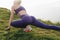 young sportswoman in stylish sportswear stretching legs on green grass on cliff Etretat