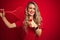 Young sportwoman playing tennis with racket and a ball over red isolated background happy with big smile doing ok sign, thumb up