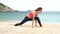 Young sporty female does stretching exercise and sit on twine split on the beach near the sea