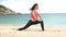 Young sporty female does stretching exercise and sit on twine split on the beach near the sea