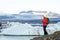 Young sporty girl with backpack admires beautiful view of the ice lake and mountains. Ice lagoon in Iceland