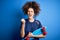 Young sporty woman with curly hair and piercing holding skate over blue background annoyed and frustrated shouting with anger,