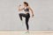 Young sporty woman doing exercise against gray background, dressed top, leggins, sneakers, has pony tail, raises legs, has intense