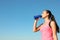 Young sporty woman drinking from water bottle outdoors on sunny day