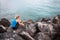 Young sporty woman runner with earphones and smartphone sitting on rocks by sea.