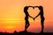 Young sporty women holding hands in heart shape at sunset