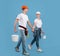 Young spouses in hardhats walking with paint equipment over blue background