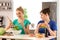 Young stout woman eating unhealthy food while her slim friend preparing salad in kitchen. Diet concept