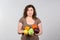 Young stout woman with fresh vegetables and fruit on grey background. Diet food concept