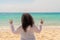 A young stout woman with long curly black hair showing fingers doing victory sign against the sea. Freedom and travel concept