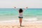 A young stout woman with long curly black hair is standing with her hands up against the sea