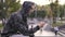 Young streetstyle man in hoodie using his smartphone in hood, Sitting on the fence of skatepark