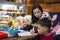 Young student doing homework at home with school books, newspaper and digital pad helped by his mother. Mum writing on the