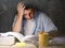 Young student at home desk reading studying at night with pile of books and coffee