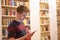 Young student in library uses his phone in front of bookshelf