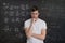 Young student is solving math exam. Mathematics formular on blackboard in background