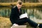 Young student is studying on the nature in the park near the lake. a guy in a black suit and red tie reads a laptop and