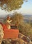 Young stylish bald male saxophonist sits on an orange sofa in mountains of Cyprus in nature, under pine tree, holds an alto