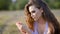 Young stylish brunette using smartphone while posing on background of country field.