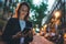 Young stylish business woman writes message on smartphone walking evening city street, hipster tourist traveling in european town