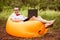 Young stylish freelancer man in glasses working at laptop sitting on Inflatable mattress in garden. Online education