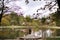 Young stylish groom and bride in luxury long dress standing in front of the lake in park with blooming cherry or sakura blossoms