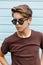 Young stylish handsome hipster man with trendy hairstyle in fashionable brown t-shirt in black sunglasses is posing