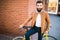 Young stylish man with a beard sitting on bicycle on a brick background