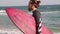 A young stylish man with a beard is standing on the beach with a surfboard