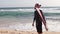 A young stylish man with a beard is standing on the beach with a surfboard