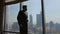 Young Stylish Man In Suit Walks Along Large Window. From The Window View Of Dubai From Height. He Stops And Looks Out