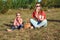 Young stylish mother blowing soap bubbles with her little cute son sitting on the grass.