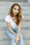 Young stylish pretty woman in trendy vintage jeans in a white stylish t-shirt is resting sitting on the steps.