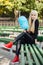 Young stylish sporty blond beautiful teen girl with cyan-blue candy-floss sitting crossed legs at park bench on a warm fall day a