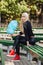 Young stylish sporty blond beautiful teen girl with cyan-blue candy-floss sitting crossed legs at park bench on a warm fall day a