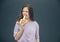 Young stylish trendy woman isolated over grey blue background. Girl biting piece of yellow ripe banana and doing weird