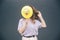 Young stylish trendy woman  over grey blue background. Girl hiding her face behind yellow ballon with funny
