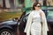 Young stylish woman gets out of the car. In winter, a girl driver in a white fur coat and sunglasses near her car.