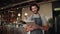 Young successful cafe owner standing in cafe wearing black striped apron using digital tablet while accepting online