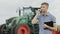 A young successful farmer communicates by phone. It stands against the background of a large tractor