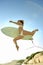 Young surfer jumping onto beach with board under arm